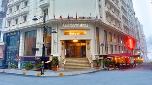 Un hotel de varios pisos con una entrada destacada, balcones y un toldo rojo.