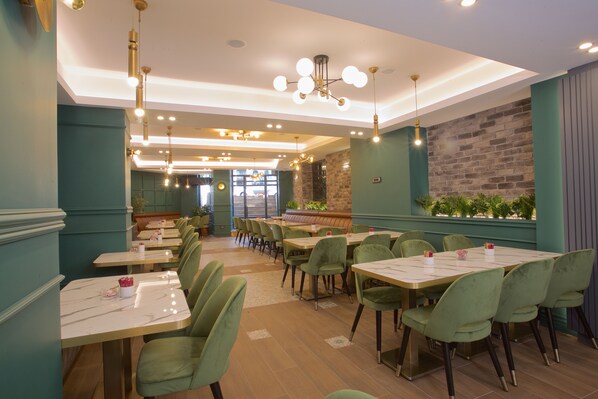 Restaurante com cadeiras verdes, mesas de mármore e parede de tijolos.
