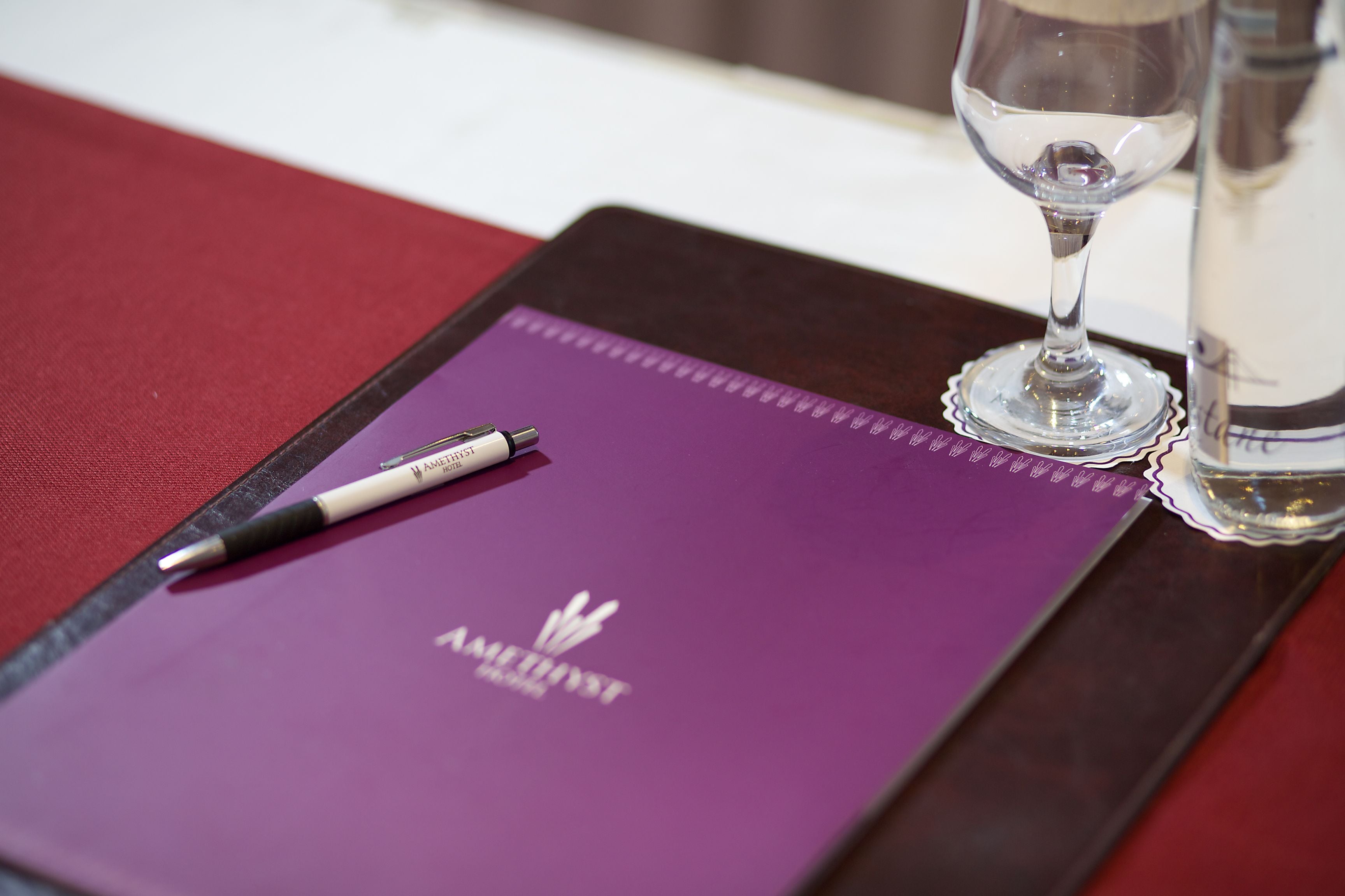 Ein violettes Notizbuch mit Stift und einem Glas Wasser auf einer Holzschale.