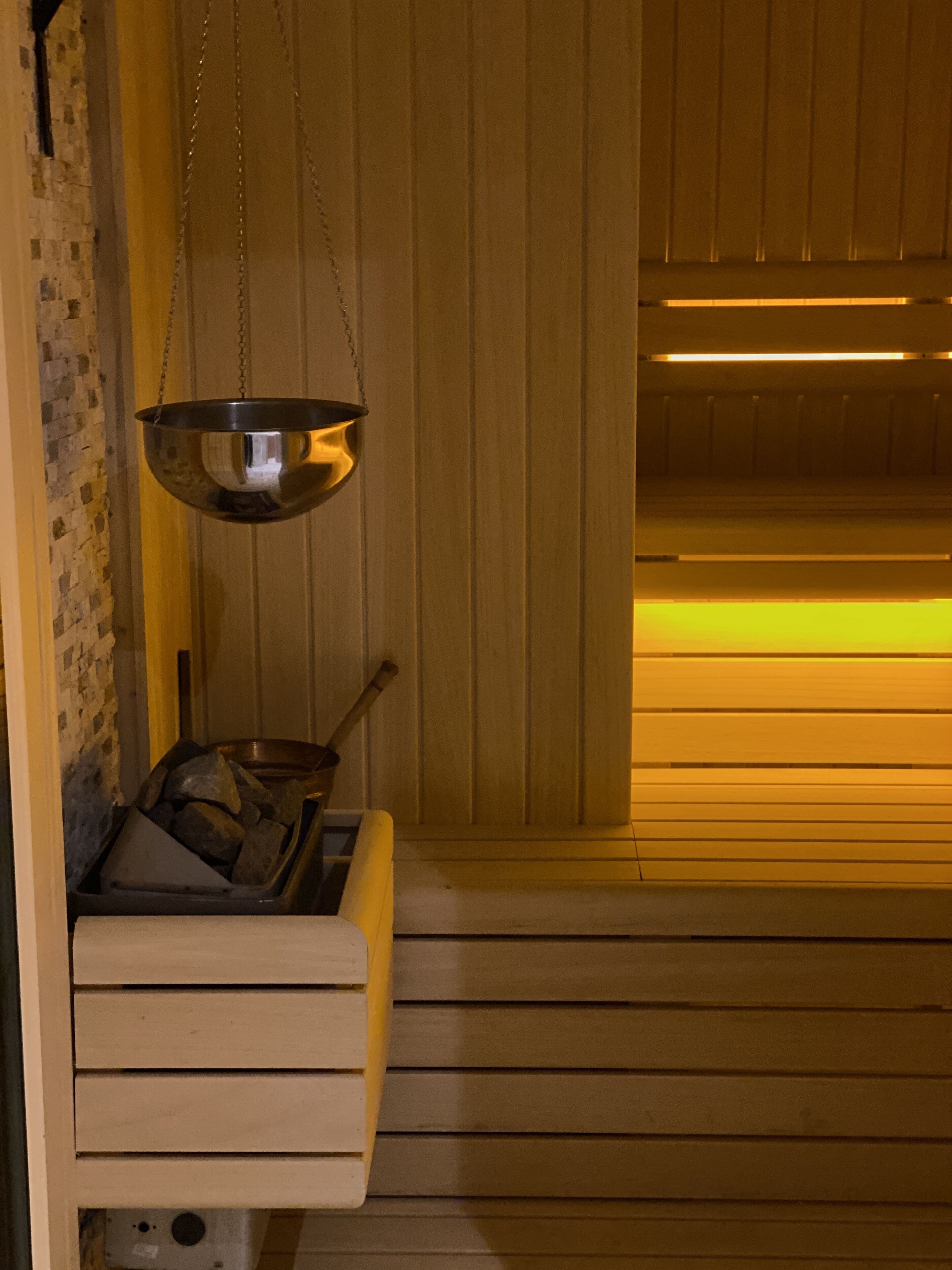 Una sala de sauna con un banco de madera, un recipiente metálico colgante y una pared de madera.