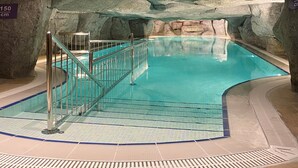 Una piscina interior con agua azul cristalina, rodeada de muros de piedra y suelo de baldosas.