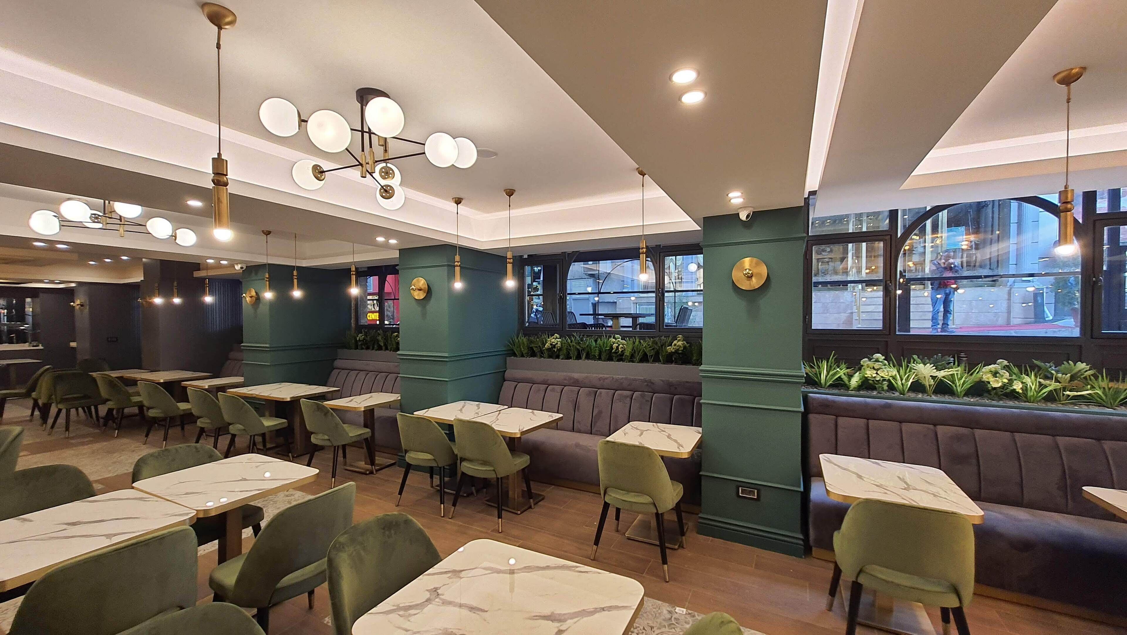 A restaurant interior with green upholstered booths, marble-topped tables, and pendant lighting.