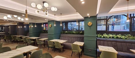 A restaurant interior with green upholstered booths, marble-topped tables, and pendant lighting.
