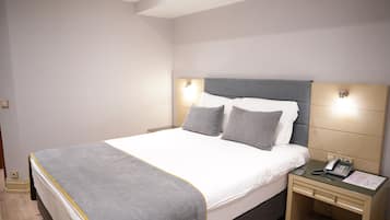 Una cama bien hecha con un edredón gris y blanco, un teléfono en la mesita de noche y una pequeña mesa de noche con una lámpara.