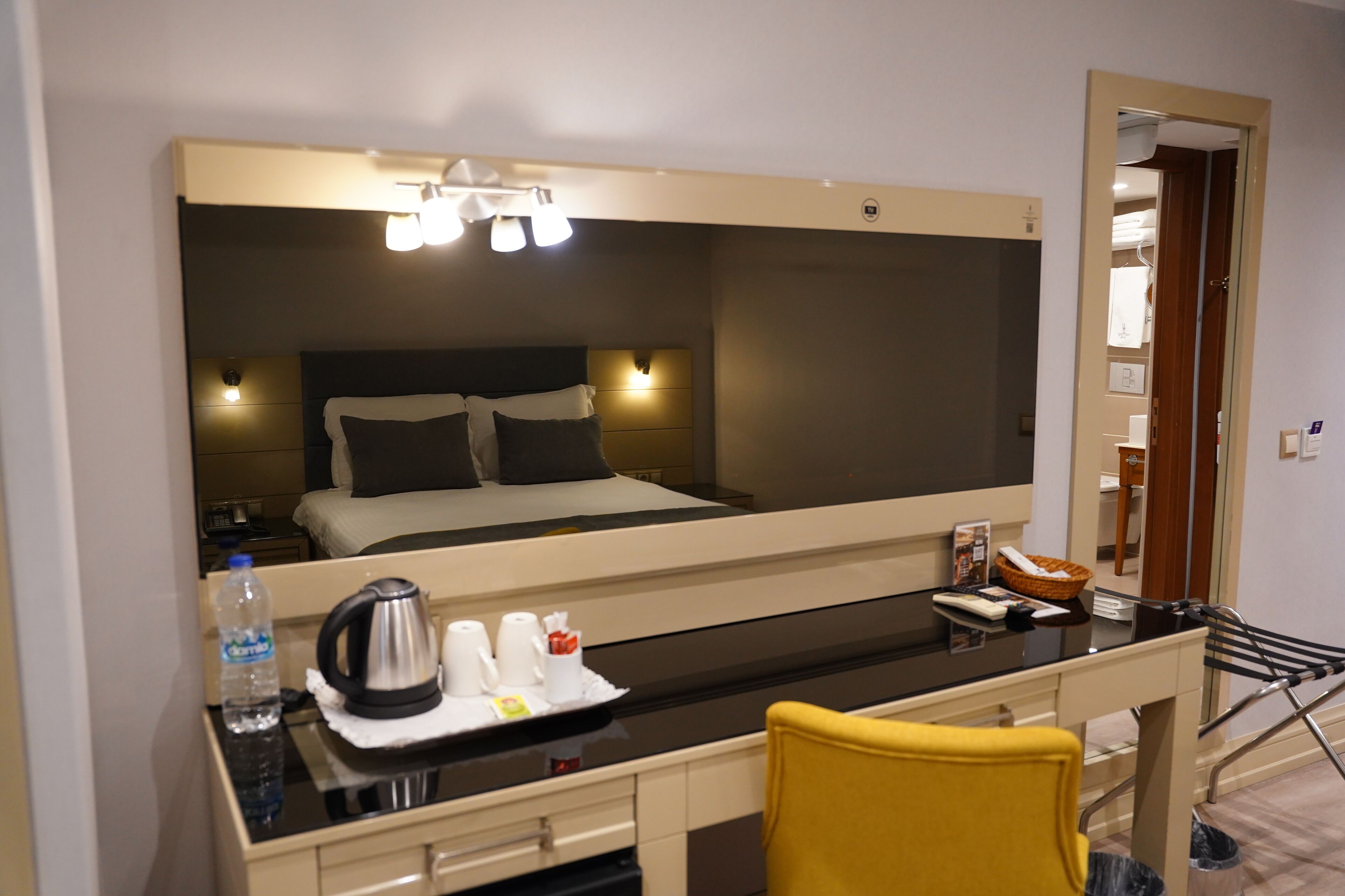 A hotel room with a bed, bedside table, and a mirror.