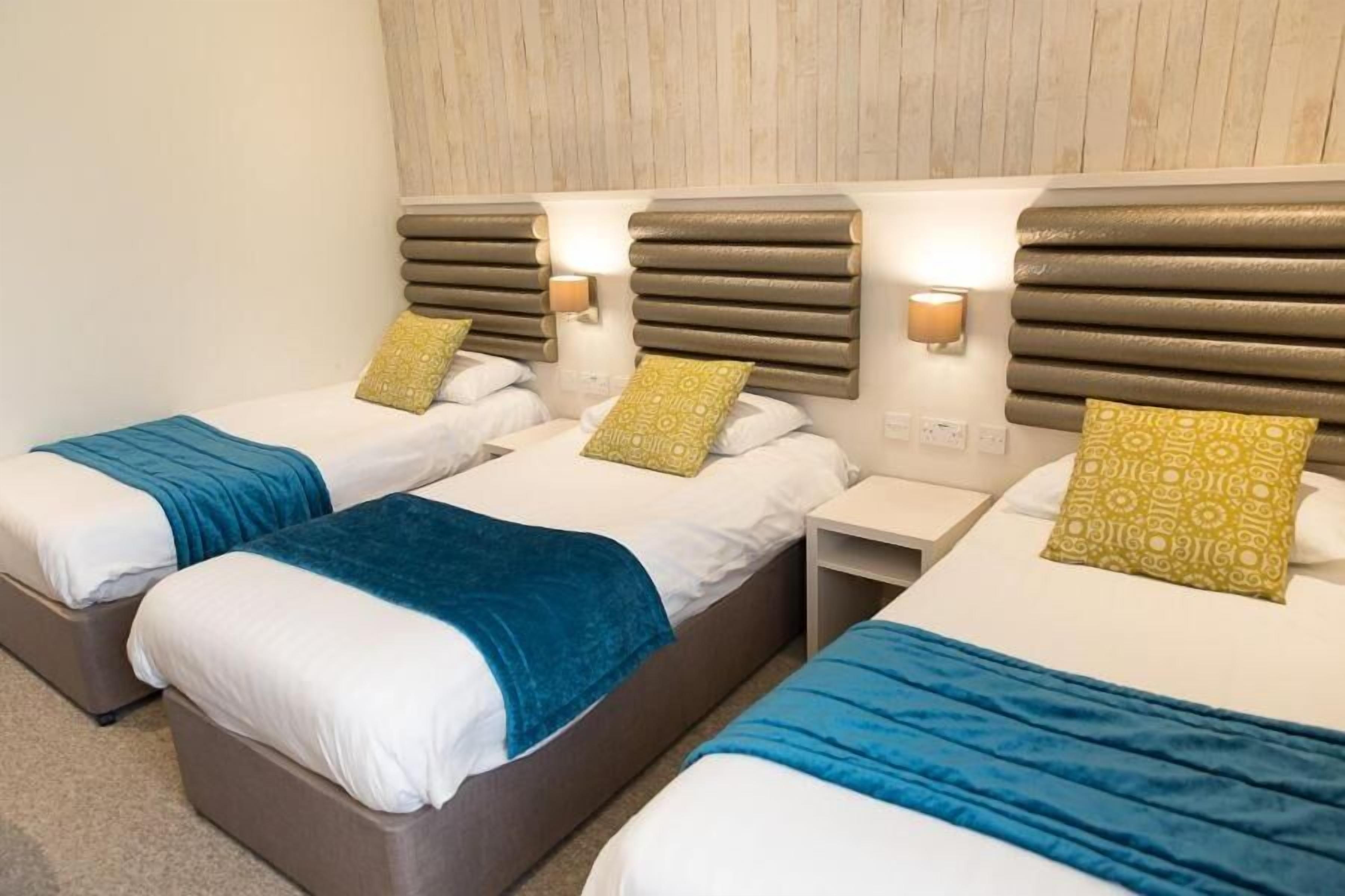 A hotel room with three beds, each with a headboard, bedside tables, and lamps.