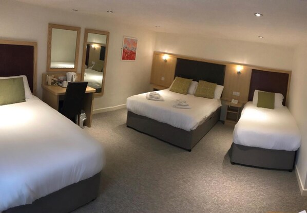 A hotel room with three beds, a desk, and a chair.