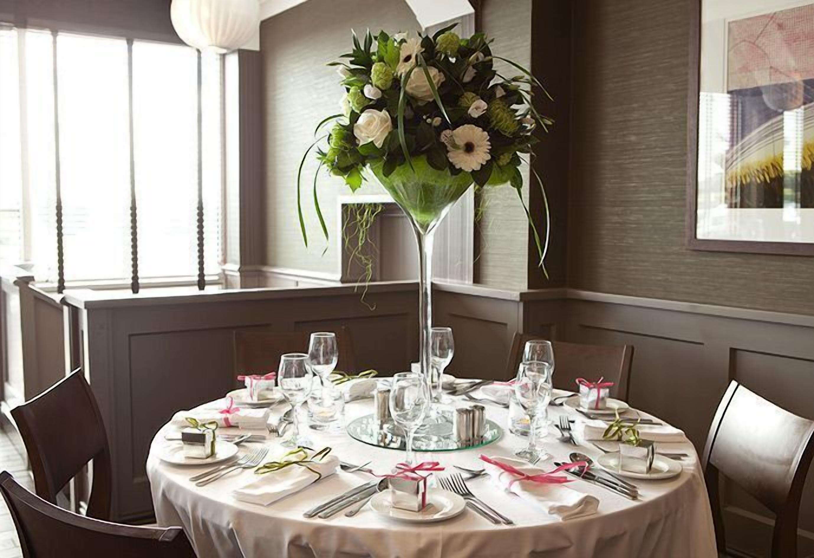 A round dining table set for four with a floral centerpiece, white tablecloth, and neatly arranged cutlery.