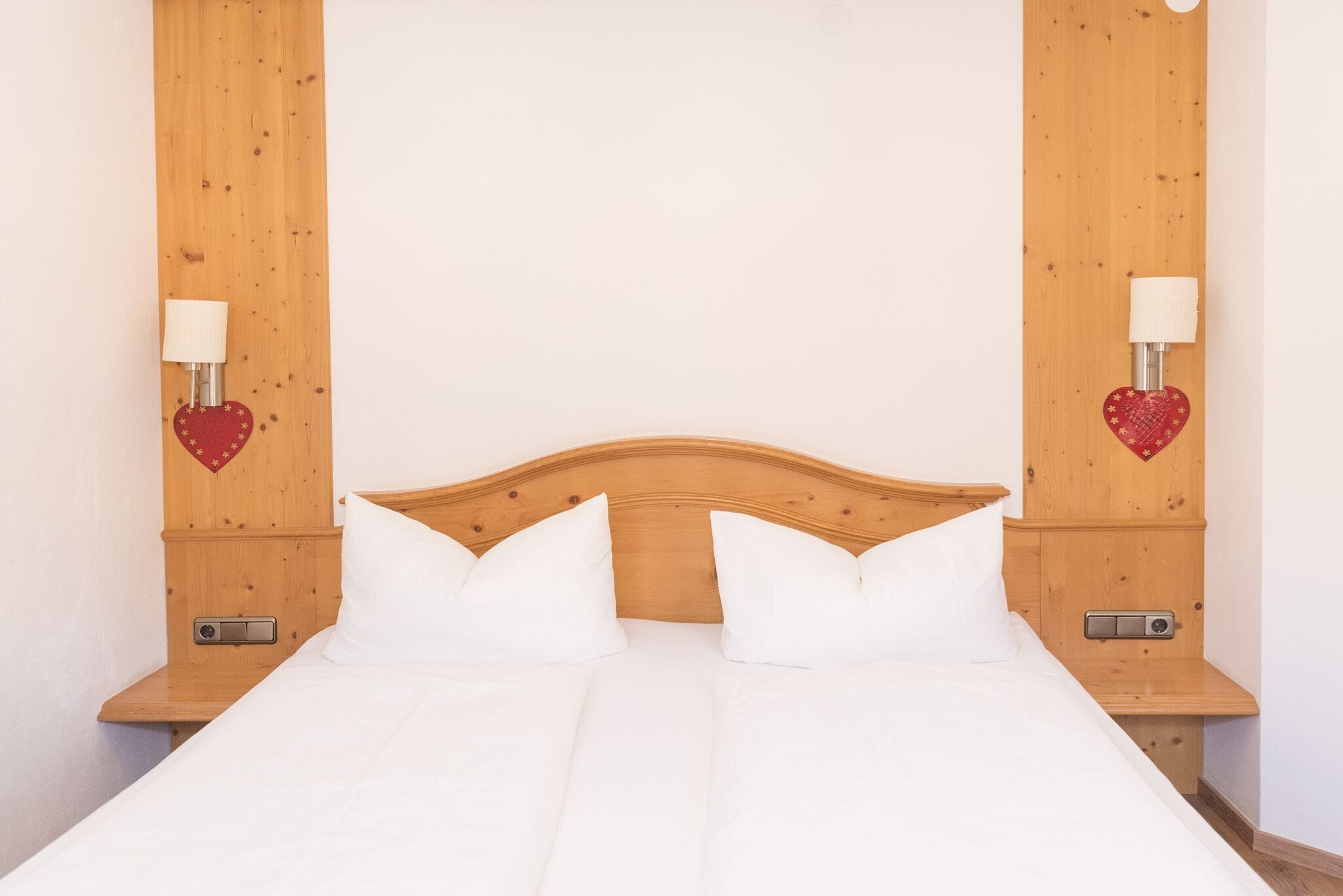 A neatly made bed with white linens and two heart-shaped wall decorations.