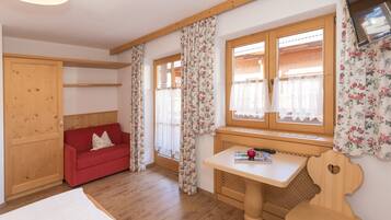 Ein gemütliches Zimmer mit Holzwänden, einem roten Sofa, einem Holztisch und einem Fenster mit floralen Vorhängen.