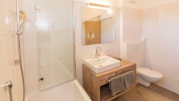 Un baño moderno con ducha envuelta en vidrio, tocador de madera con lavamanos y un inodoro.