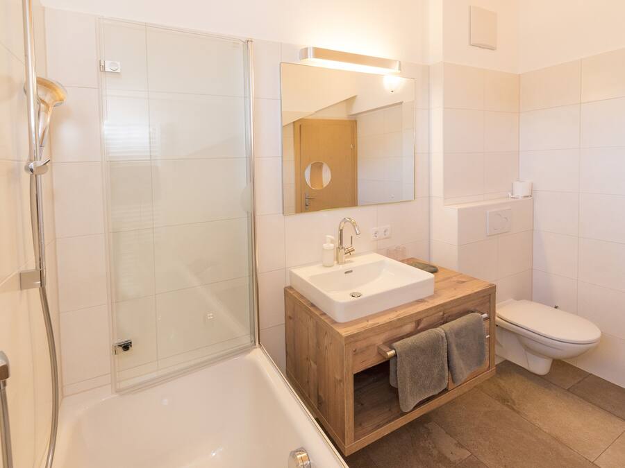 Un baño moderno con ducha envuelta en vidrio, tocador de madera con lavamanos y un inodoro.