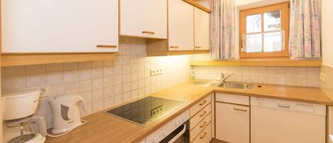 A kitchen with white cabinets, a wooden countertop, a coffee maker, a toaster, a dishwasher, and a window with floral curtains.