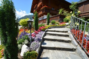 A stone staircase leading to a wooden building with balconies, surrounded by colorful flower beds and greenery. - Haus Sonnwend (Alpbach)