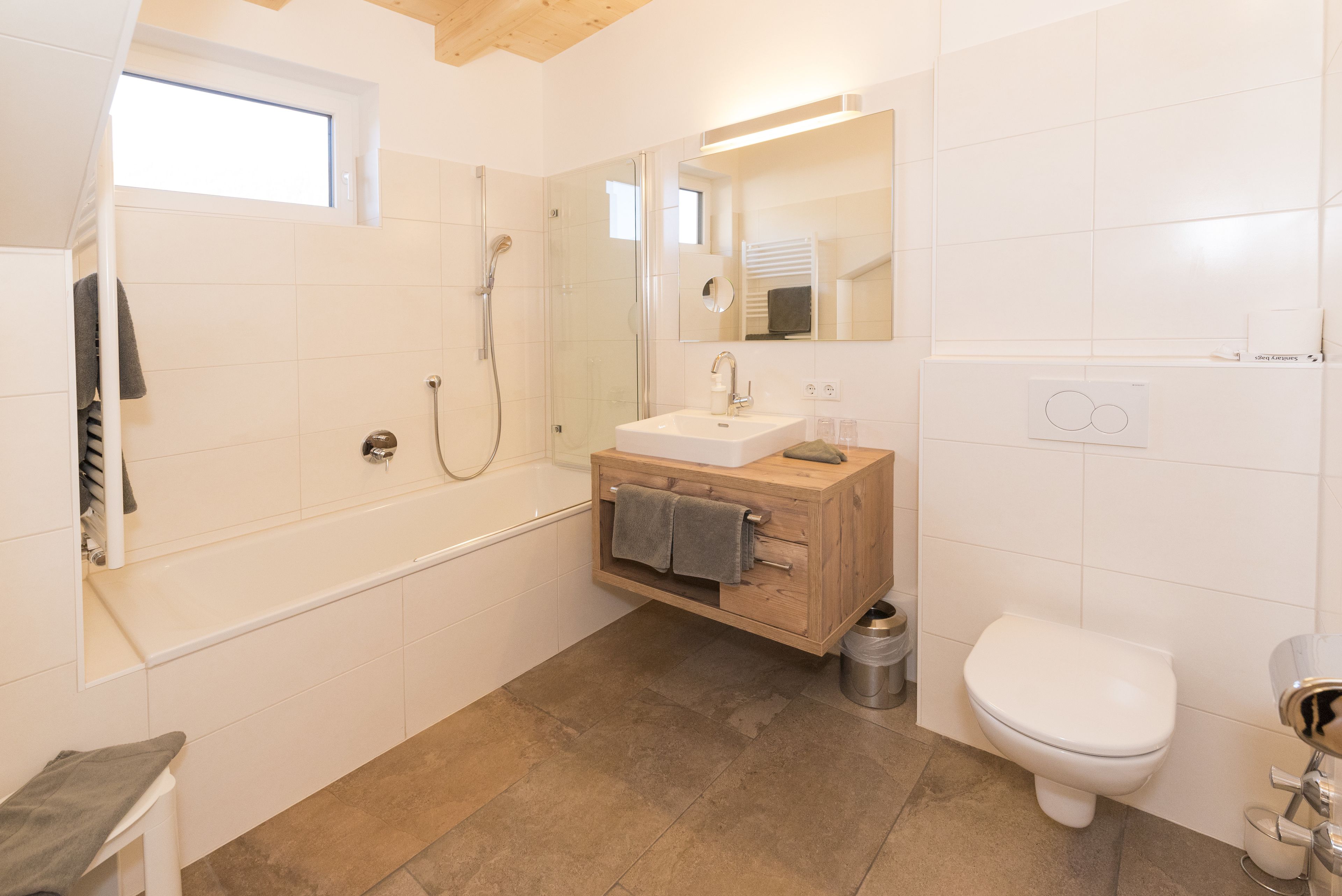 A modern bathroom with a bathtub, a wooden vanity, a toilet, and a glass-enclosed shower.