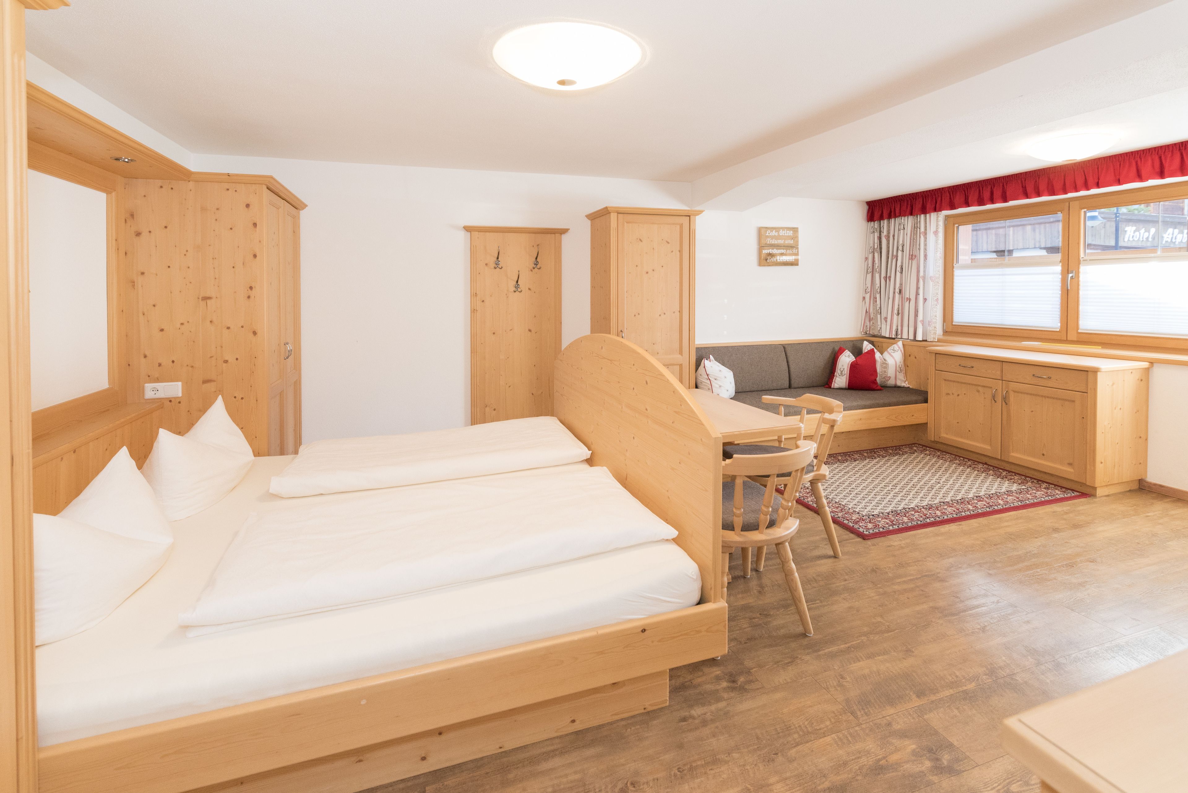 Ein Zimmer mit einem hölzernen Bett, einem Schreibtisch aus Holz, einem Fenster mit Vorhängen und einem Holzschrank.