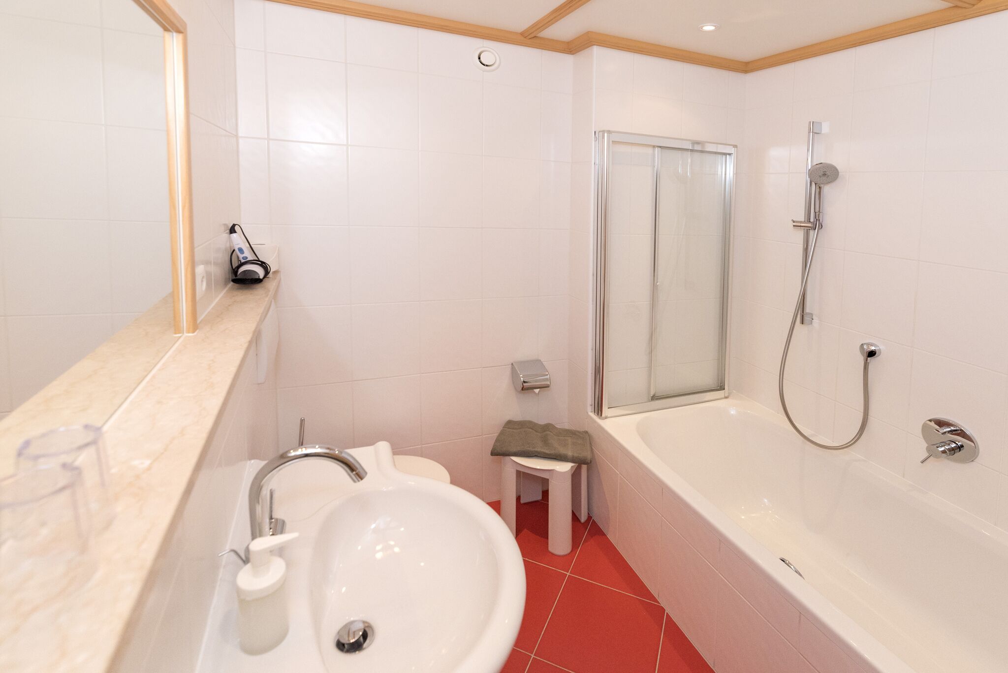 Een moderne badkamer met een wastafel, toilet, douche en een klein krukje.