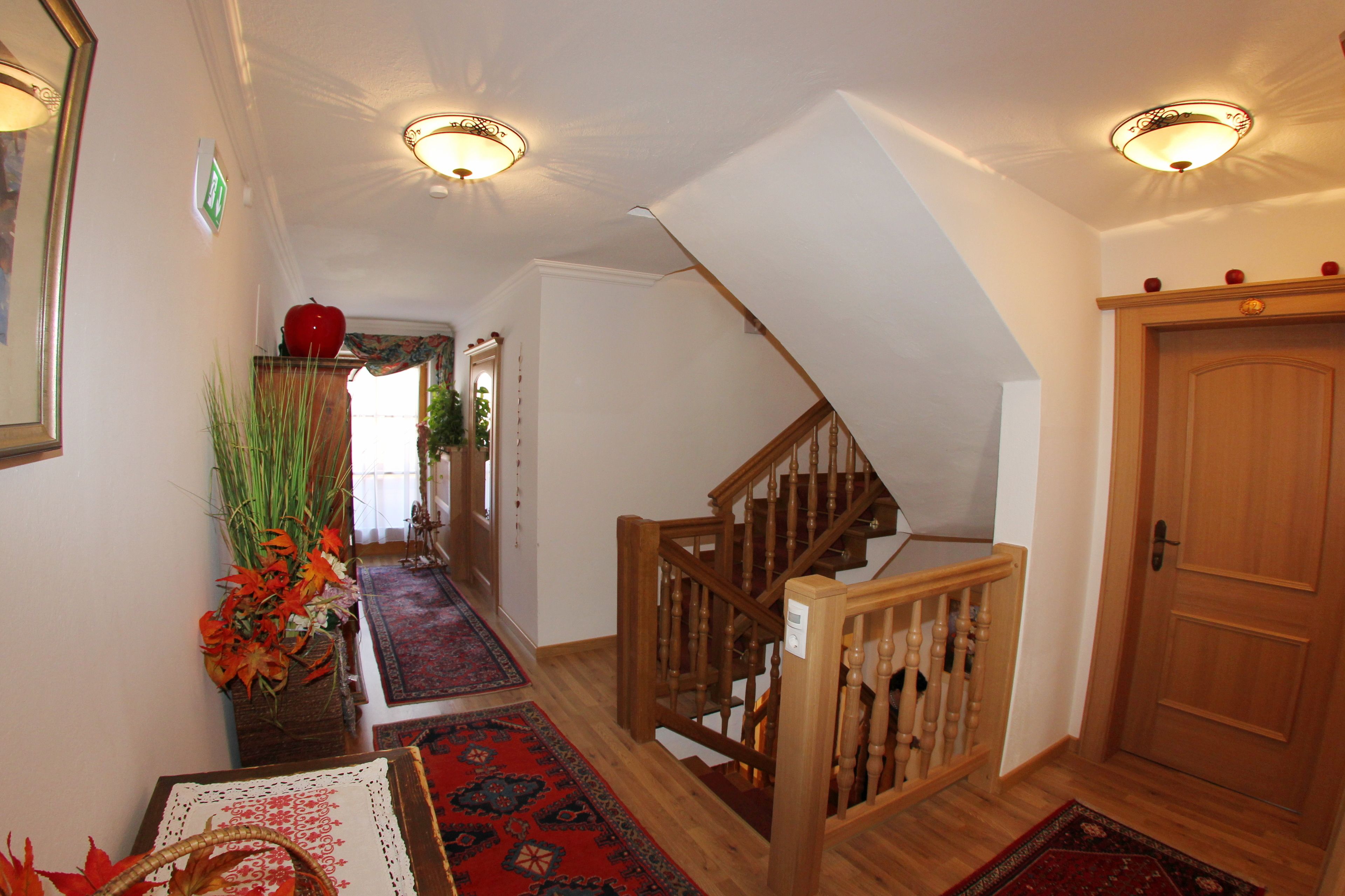 A hallway with a wooden staircase, a red apple on a shelf, and a patterned rug.