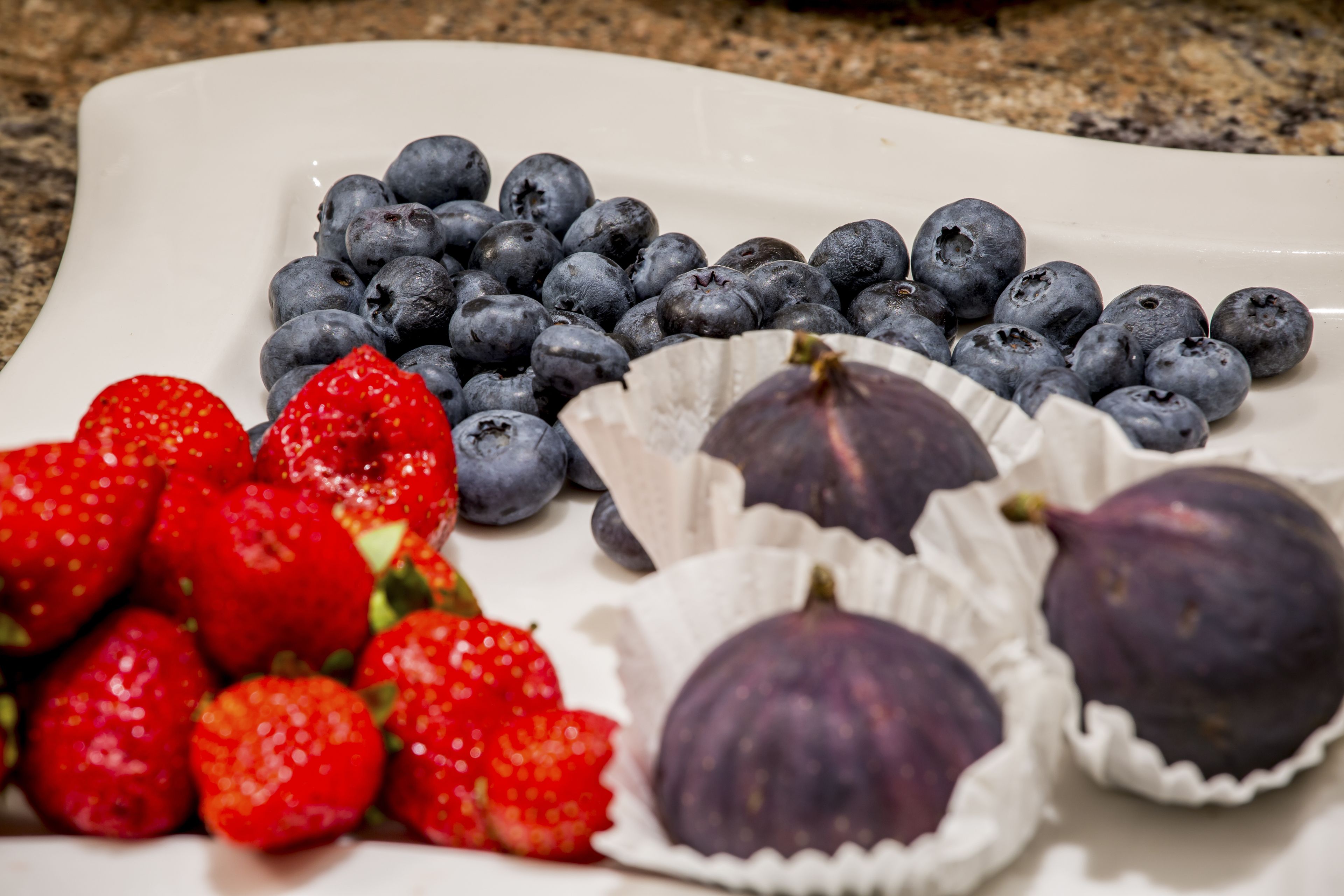 A white plate with strawberries, blueberries, and figs.