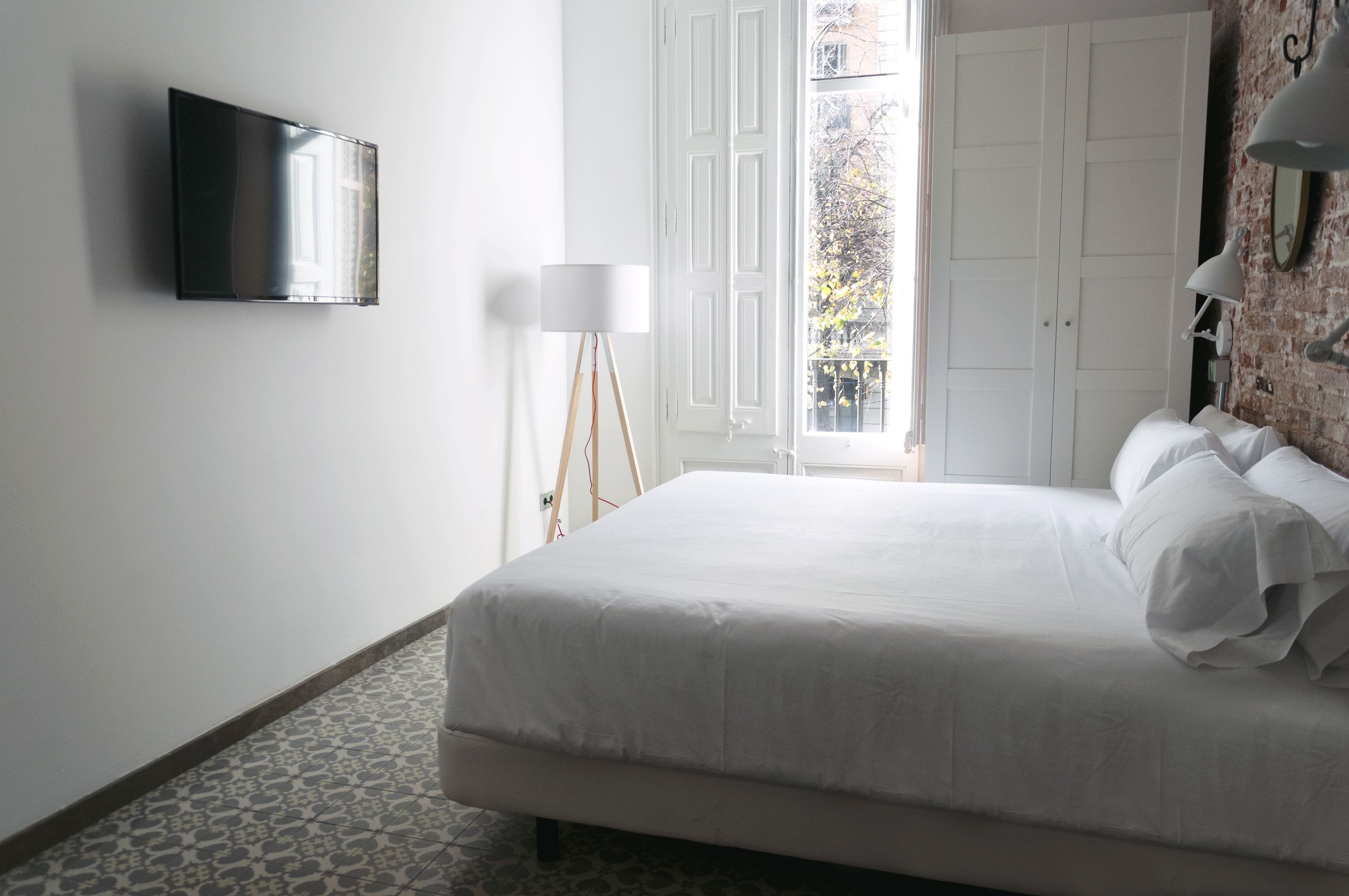 Quarto com cama, TV de tela plana na parede, abajur e vista para o exterior através de uma porta.