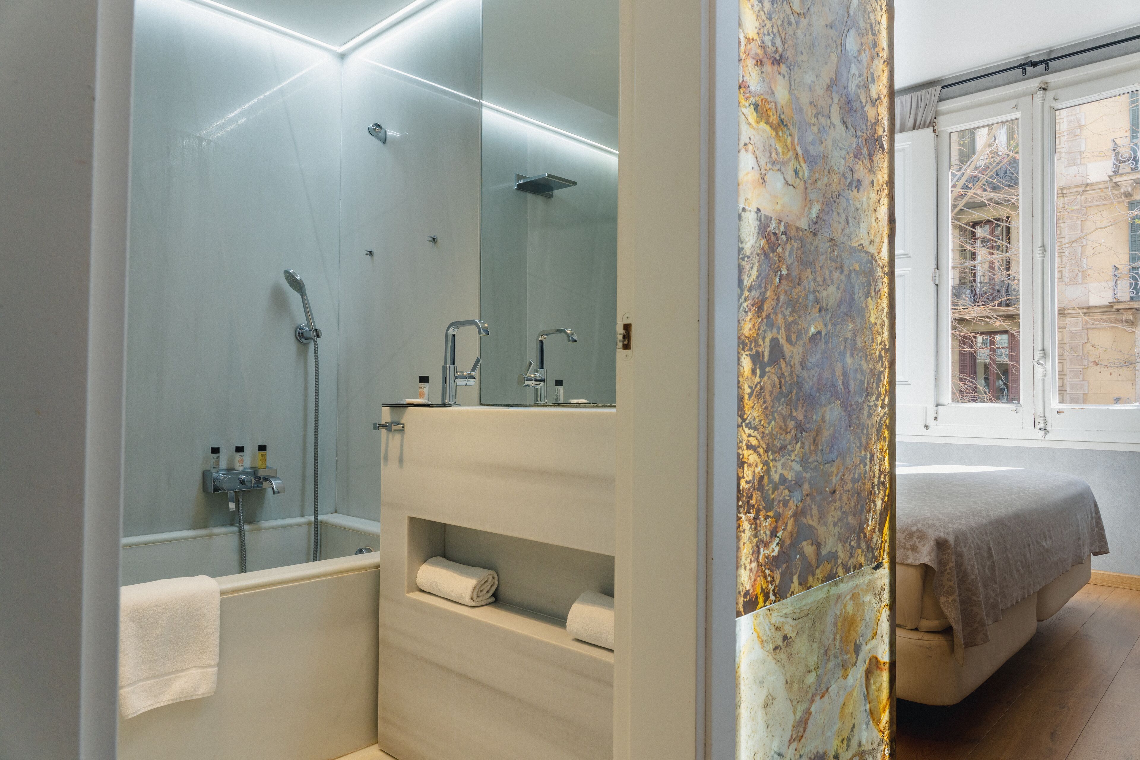 Un baño moderno con ducha de vidrio, tocador con espejo y cama con vista a la ciudad.