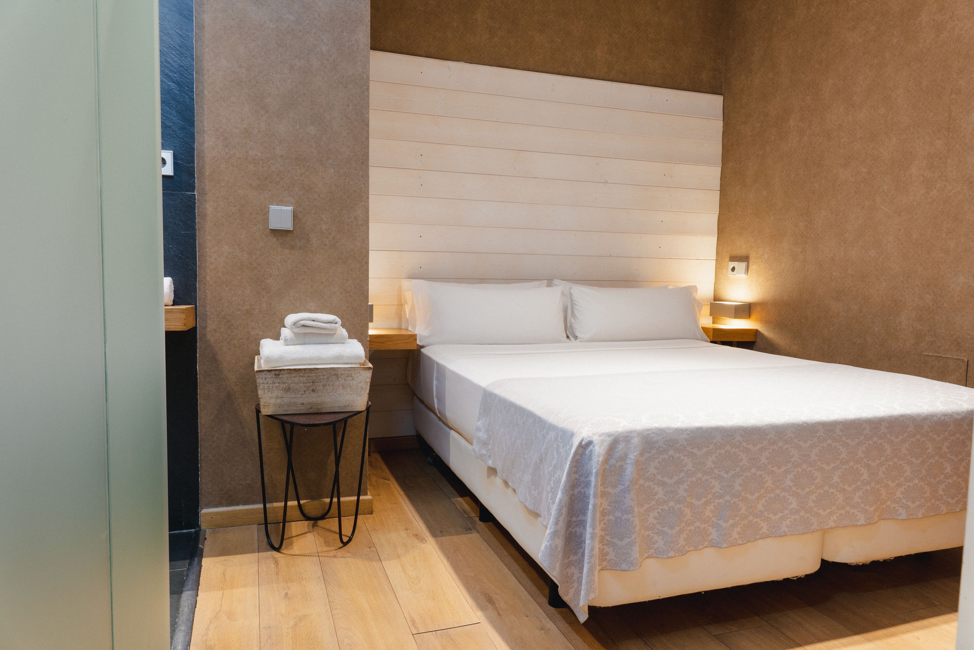 Una camera da letto con un letto, un comodino, un tavolino con degli asciugamani e una lampada a parete.