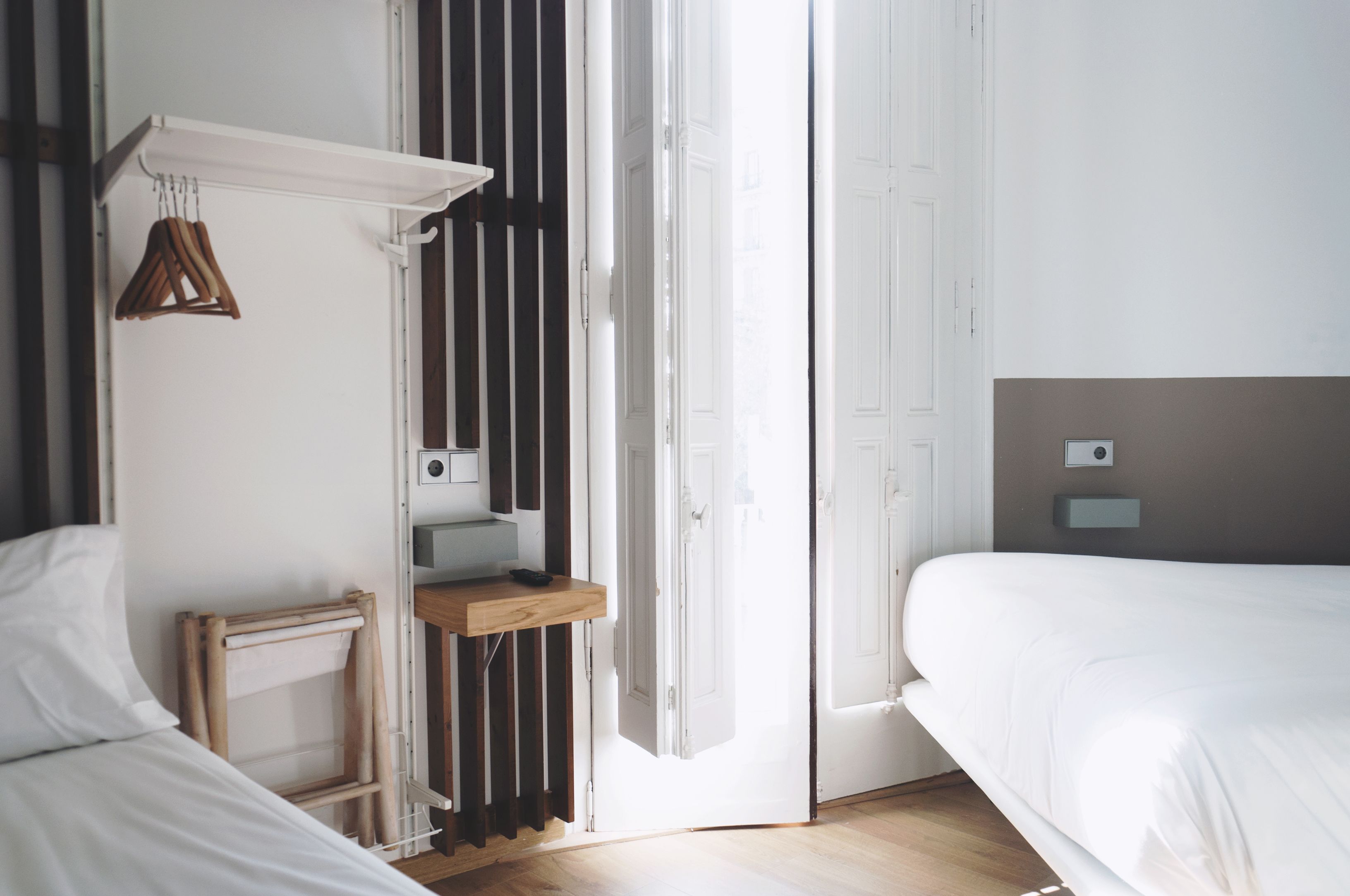 Un dormitorio moderno con un ventanal grande, una mesita de noche de madera, una lámpara colgante y una estantería empotrada.