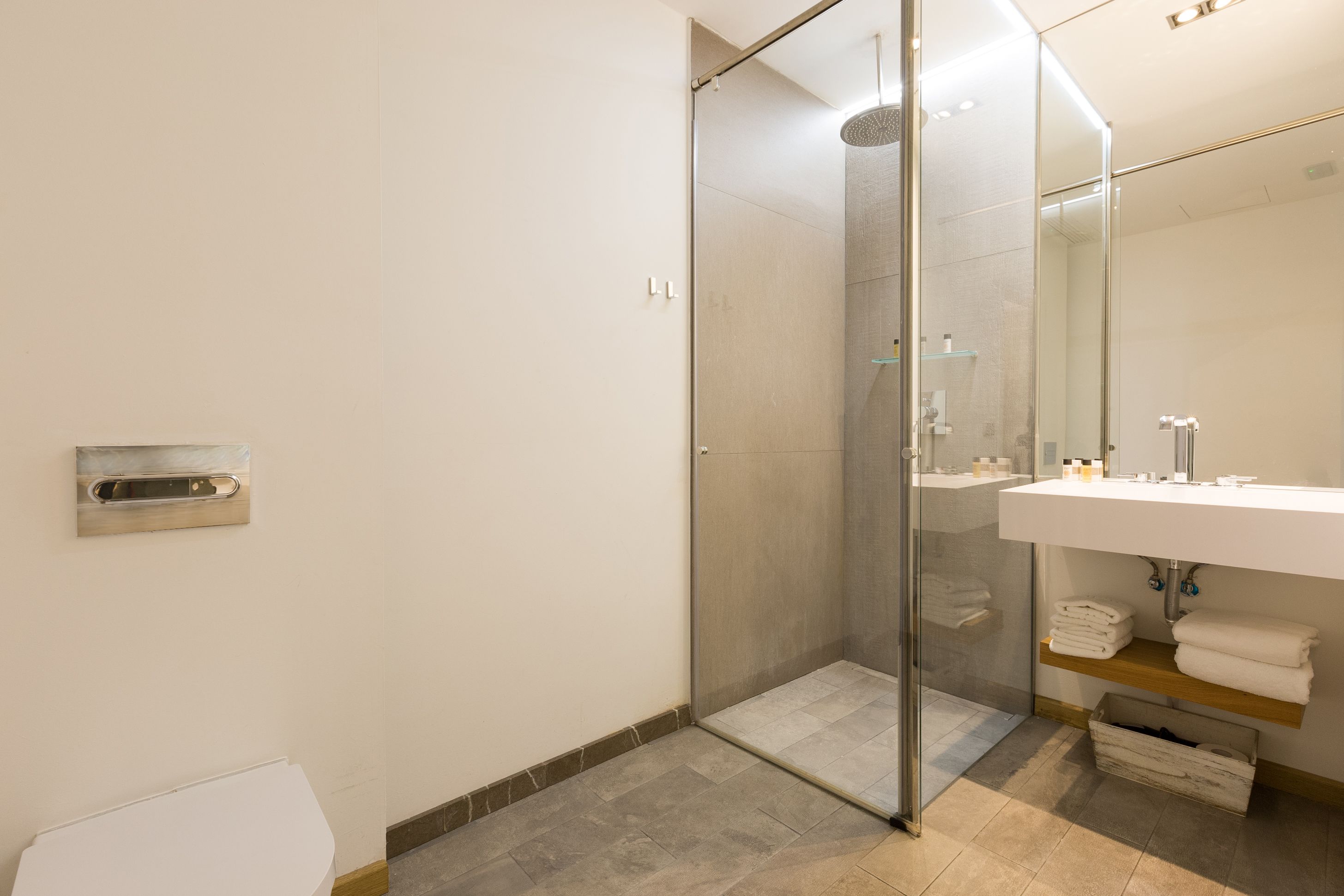 Un baño moderno con ducha de vidrio, un lavamanos blanco con espejo y toallas ordenadas en un estante.