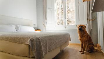 Un dormitorio con cama, ventana y un perro sentado junto a la ventana.
