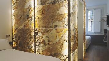 A bedroom with a marble wall, a bed, a nightstand, and a window with a view.