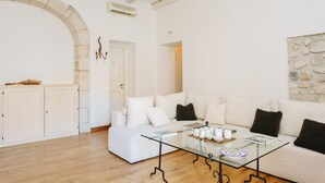 A modern living room with a glass coffee table, white sofas, a stone archway, and a stone wall. - Palazzo del Sale (Syracuse)