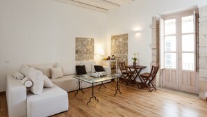 A modern living room with a glass coffee table, a white sofa, and a dining area with wooden chairs. - Palazzo del Sale (Syracuse)