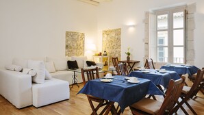 A dining area with tables set for a meal, a sofa, and a stone wall. - Palazzo del Sale (Syracuse)
