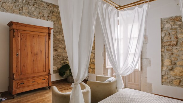 A bedroom with a stone wall, wooden cabinet, and a bed with white bedding. - Palazzo del Sale (Syracuse)