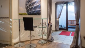 A modern hotel lobby with a glass table, a black chair, a large abstract painting, and a view of the outside balcony. - Garden House   & Eastpark Apartments (Munich)