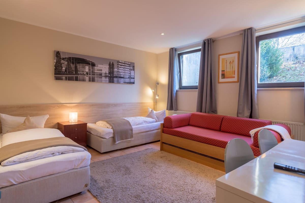 Een hotelkamer met twee bedden, een rode bank, een bureau en een raam met gordijnen.