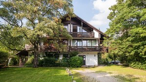 A two-story wooden house with a balcony, surrounded by lush greenery and a clear sky. - Garden House   & Eastpark Apartments (Munich)
