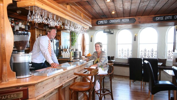 Zona de bar con mobiliario de madera, una máquina de café y un panel con el menú de café y espresso.