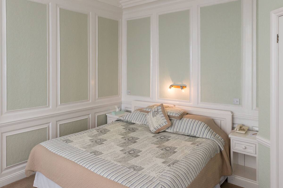 A bedroom with a large bed, a nightstand, and a wall-mounted light.