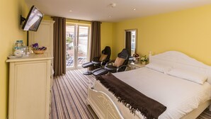 Habitación de hotel con cama, escritorio con silla, televisor montado en la pared y ventana con cortinas.