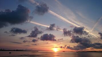 Un coucher de soleil sur une étendue d’eau calme, avec quelques nuages épars et des traînées de condensation.