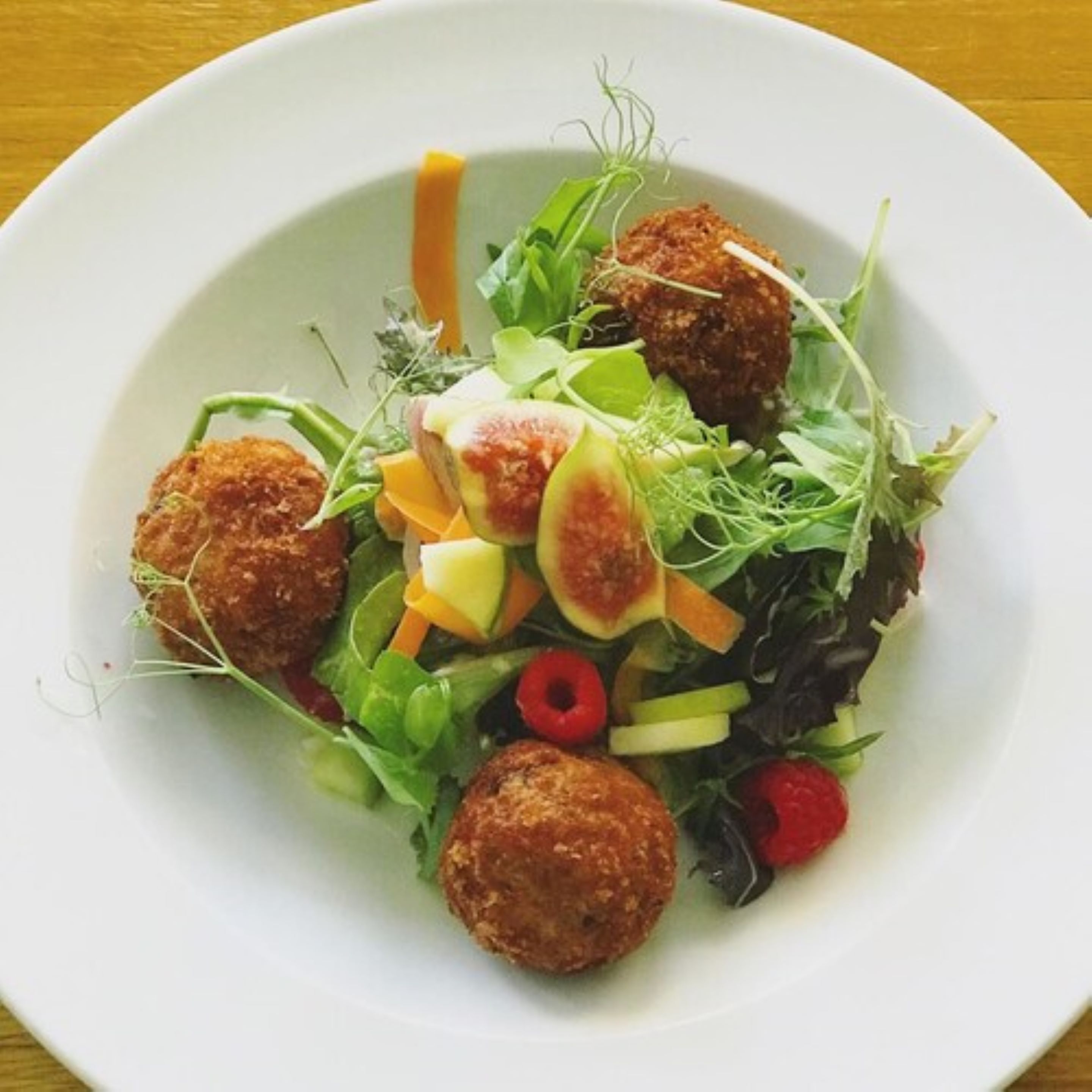 A white plate with a salad containing greens, apple slices, and red berries, accompanied by two round, breaded items.