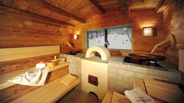 Una cabaña de madera con sauna, bancos y chimenea de piedra.