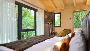 Un dormitorio con una cama grande, una manta de piel sintética y vistas a árboles por la ventana.