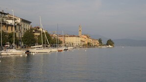 A marina with boats docked, buildings along the waterfront, and a prominent tower in the background. - Concept Village Piccola Gardiola (San Felice del Benaco)