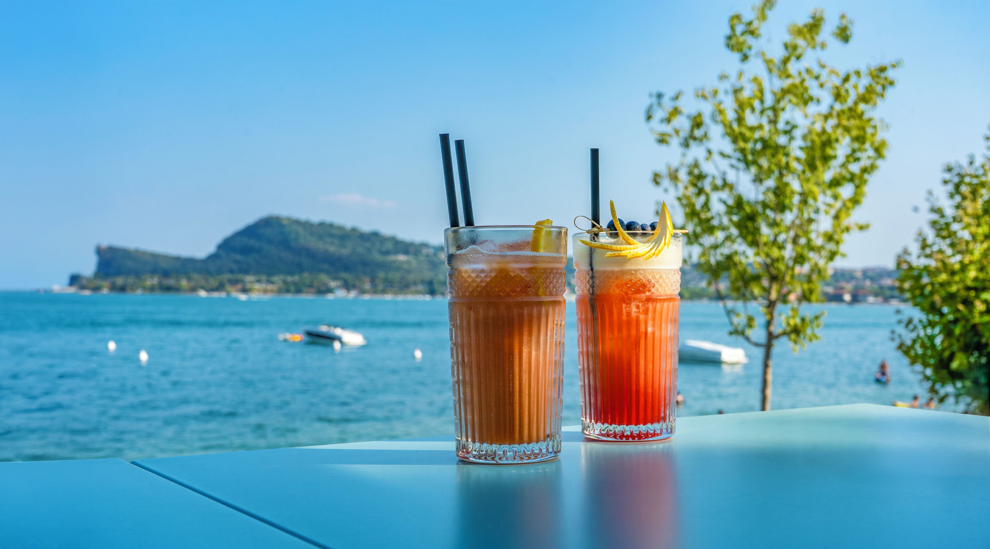 Two drinks on a table with a view of the sea and boats in the background.