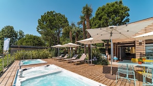 A wooden deck with two hot tubs, lounge chairs, umbrellas, and a table with chairs. - Concept Village Piccola Gardiola (San Felice del Benaco)