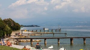 A waterfront area with a pier extending into the water, surrounded by rocks and greenery. - Concept Village Piccola Gardiola (San Felice del Benaco)