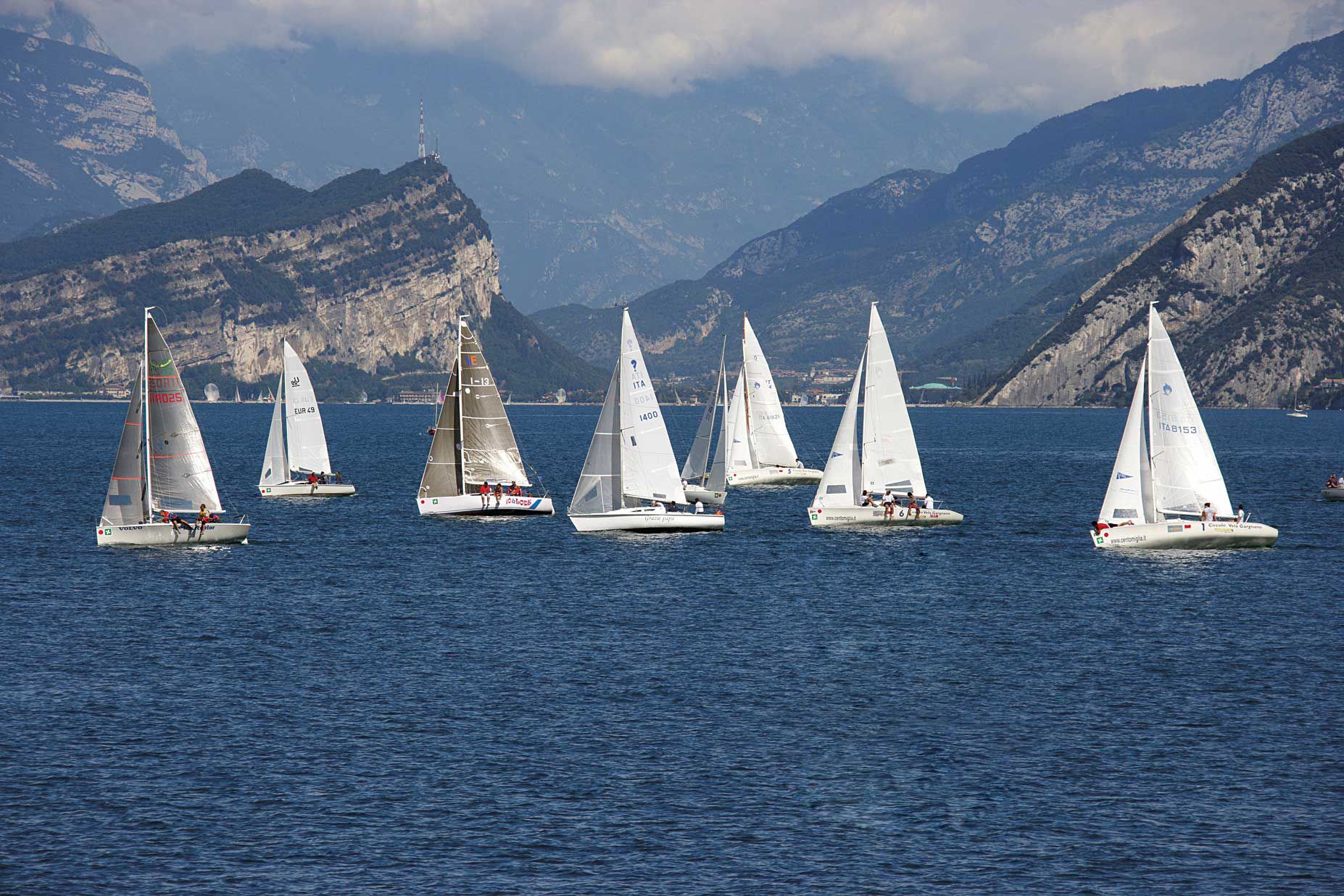 Un gruppo di vele a vela su un mare calmo, con montagne sullo sfondo.