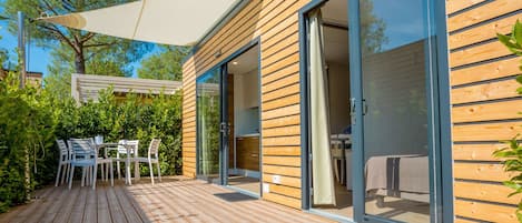 A modern outdoor patio with wooden decking, a table with chairs, and a large sliding glass door leading to a room.